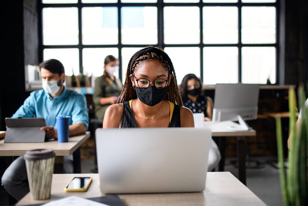 Портрет молодых бизнесменов в масках, работающих в помещении офиса. - Фото, изображение