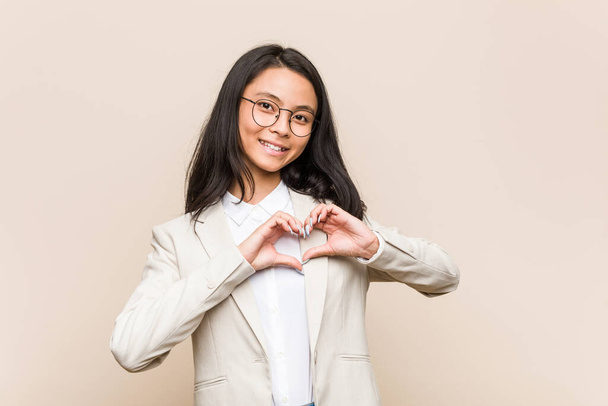 Νεαρή Κινέζα επιχειρηματίας χαμογελά και δείχνει ένα σχήμα καρδιάς με τα χέρια. - Φωτογραφία, εικόνα