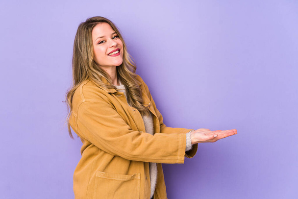 Young caucasian woman isolated on purple background holding a copy space on a palm. - Foto, Imagen