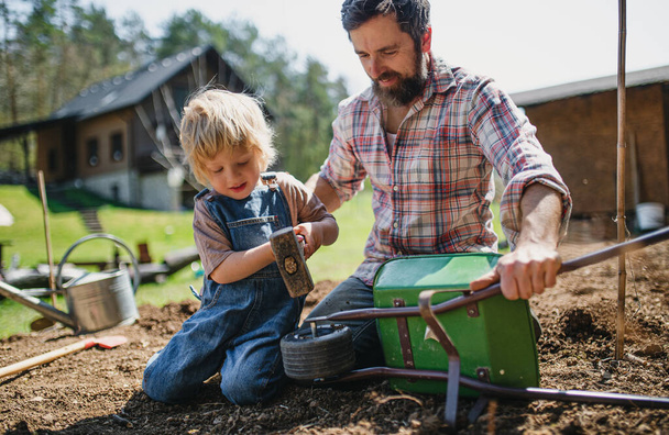 Father with small son working outdoors in garden, sustainable lifestyle concept. - Foto, Imagen