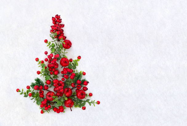 Świąteczne dekoracje. Czerwone choinki wykonane z czerwonych jagód i małych czerwonych jabłek na śniegu z miejscem na tekst. Widok z góry, płaski - Zdjęcie, obraz