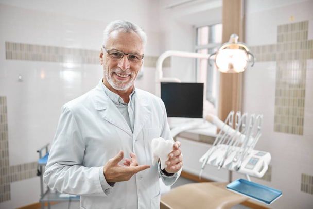 Joyful dentist holding a big molar tooth model - Фото, изображение