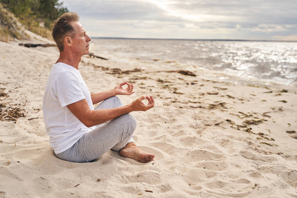 Hombre maduro meditando por la mañana en la playa - Foto, Imagen