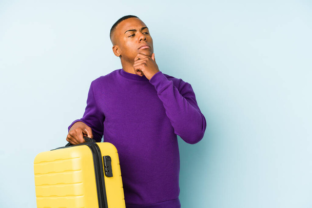Fiatal utazó férfi kezében egy bőrönd elszigetelt néz oldalra kétes és szkeptikus kifejezés. - Fotó, kép