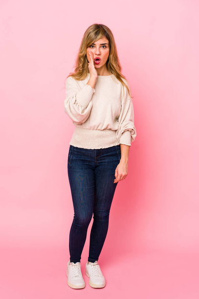 Young blonde caucasian woman standing over a pink background is saying a secret hot braking news and looking aside - Fotografie, Obrázek