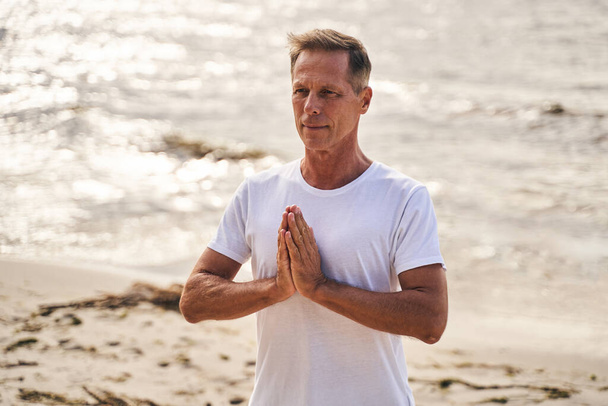 Tranquil mature man doing meditation in beach - Photo, Image