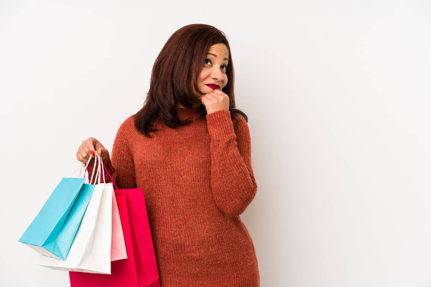 Middle age latin woman holding a shopping bags isolated looking sideways with doubtful and skeptical expression. - Photo, Image