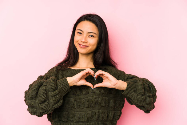 Mladá Číňanka izolované na růžovém pozadí s úsměvem a ukazující tvar srdce s rukama. - Fotografie, Obrázek