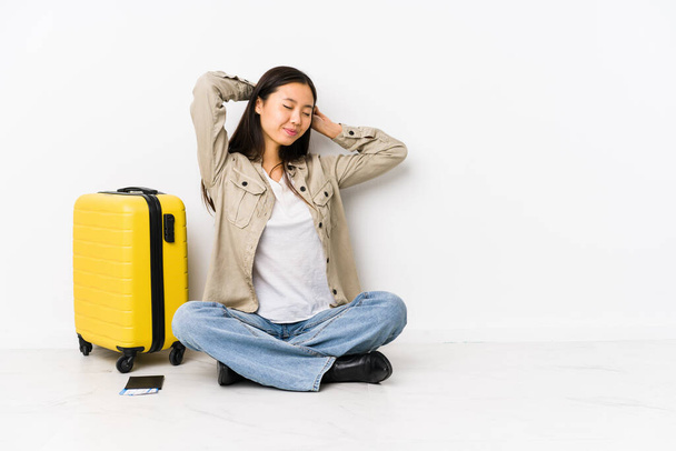Joven viajera china sentada sosteniendo una tarjeta de embarque estirando los brazos, posición relajada. - Foto, Imagen