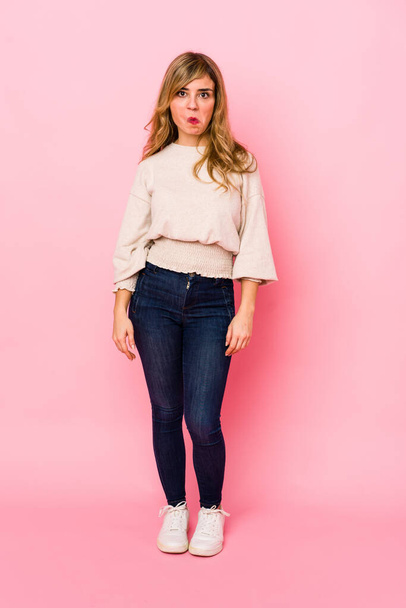 Young blonde caucasian woman standing over a pink background shrugs shoulders and open eyes confused. - Photo, Image