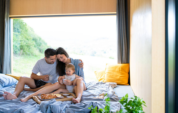 Young couple with small daughter indoors, weekend away in container house in countryside. - Foto, afbeelding