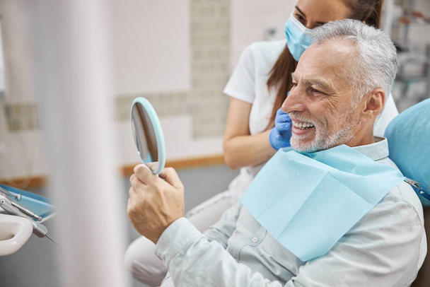 Aging patient looking in the mirror in dental office - Fotoğraf, Görsel