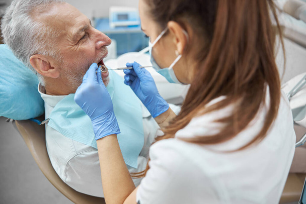 Competent female dentist examining an elderly man - Foto, afbeelding