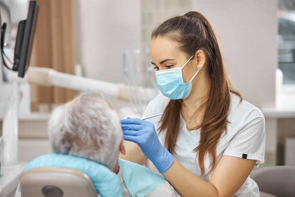 Young dental specialist treating her senior patient - Foto, immagini