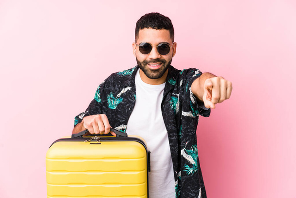 Jeune homme latino tenant une valise sourire joyeux pointant vers l'avant. - Photo, image