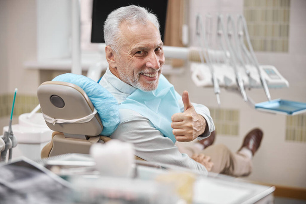 Dentistas pacientes sentados en una silla dental mostrando los pulgares hacia arriba - Foto, Imagen