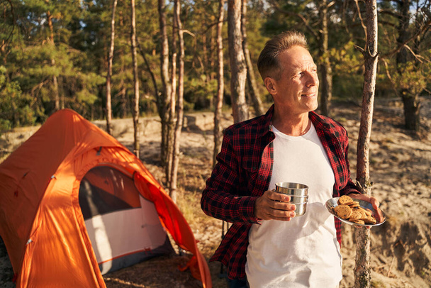Mosolygó férfi eszik reggelit közelében kemping fa - Fotó, kép