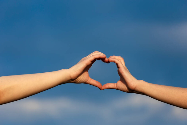 Girl hands in heart form over blue sky background - Photo, image
