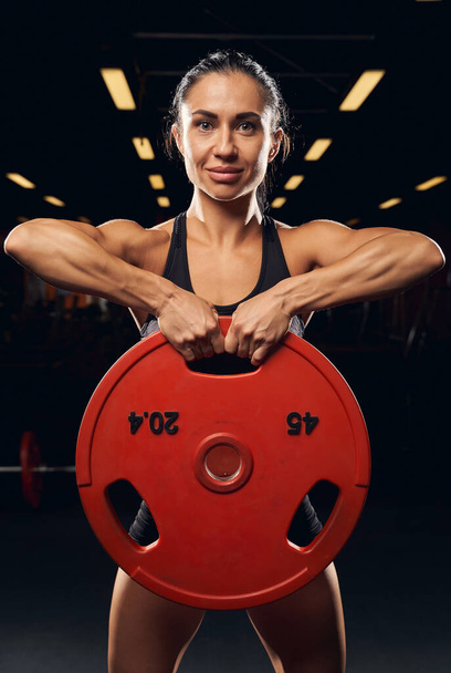 Muscly female athlete lifting weight plate with both hands - Photo, Image