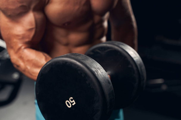 Athletic young man exercising with dumbbells at the gym - Foto, afbeelding