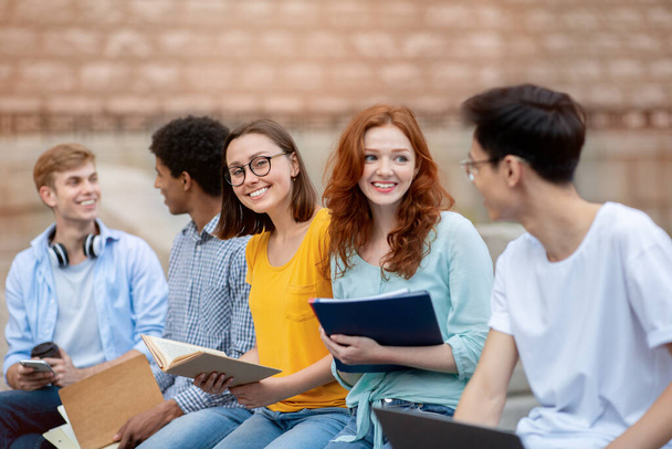 Vrolijke middelbare scholieren praten tijdens de pauze zitten en leren buiten - Foto, afbeelding