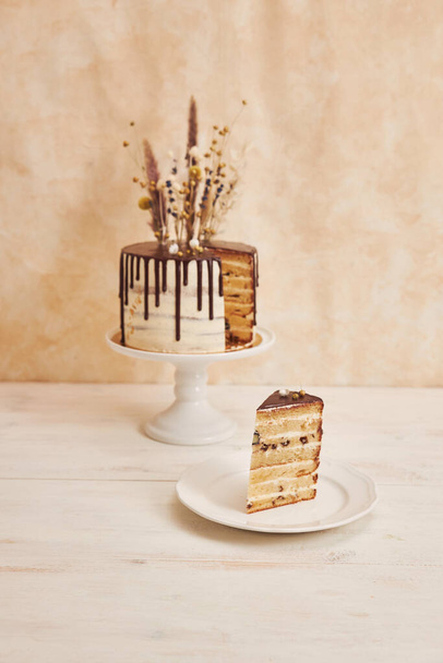 A vertical shot of delicious Boho cake with chocolate drip and flowers on top with golden decorations on a white table - Photo, image