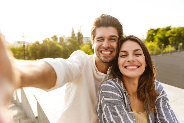 Image of young caucasian happy couple smiling and taking selfie photo while walking in park - Foto, imagen