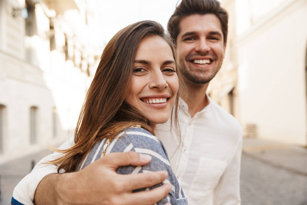 Image of young caucasian brunette couple smiling and hugging while walking on city street - Zdjęcie, obraz