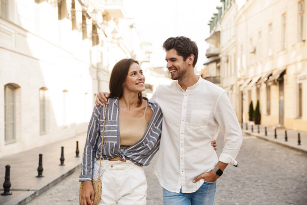 Image of young caucasian brunette couple smiling and hugging while walking on city street - Foto, imagen