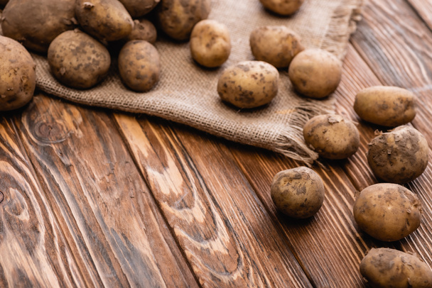 dirty potatoes and burlap on wooden table - Fotografie, Obrázek