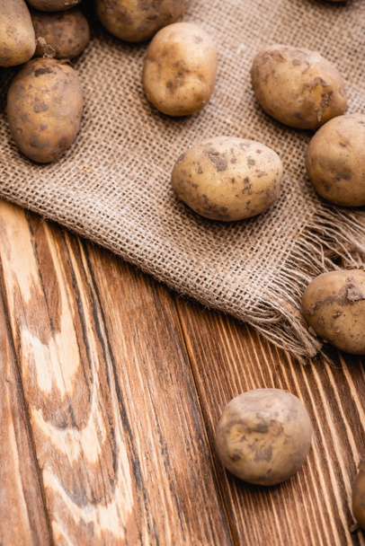 dirty potatoes and burlap on wooden table - Φωτογραφία, εικόνα