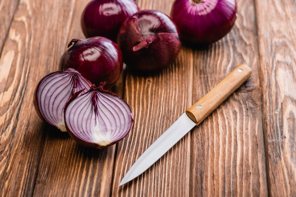 cut and whole red onion near knife on wooden table - Φωτογραφία, εικόνα