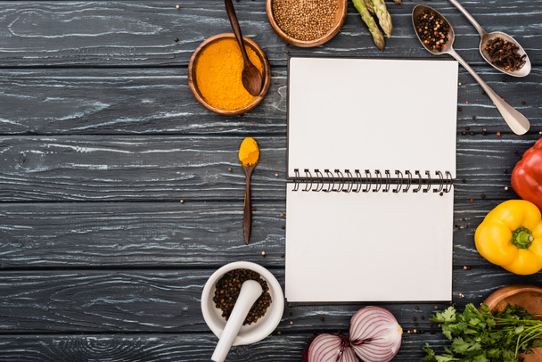 vrchní pohled na čerstvou barevnou zeleninu a koření v blízkosti prázdného notebooku na dřevěném povrchu - Fotografie, Obrázek