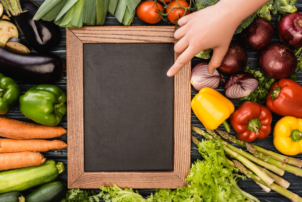 cropped view of person pointing at empty chalkboard near fresh colorful vegetables - Foto, immagini