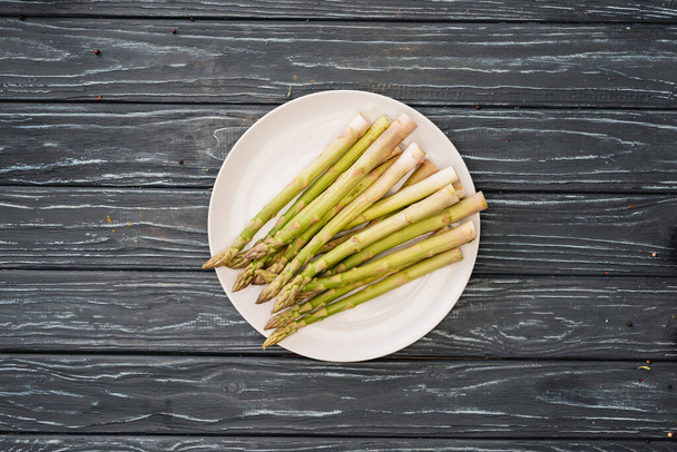 top view of fresh asparagus on plate on wooden surface - Foto, imagen
