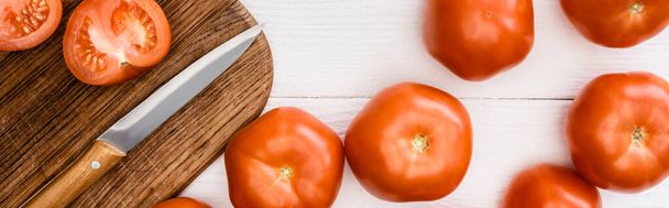 top view of ripe tomatoes on chopping board with knife on white wooden table, panoramic shot - Foto, Imagem