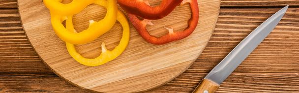 top view of colorful sliced bell peppers on wooden cutting board near knife, panoramic shot - Zdjęcie, obraz