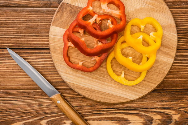 top view of colorful sliced bell peppers on wooden cutting board near knife - Foto, imagen