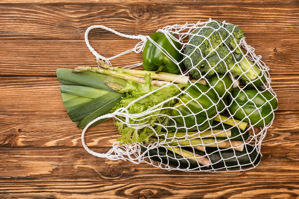 top view of fresh green ripe vegetables in string bag on wooden table - Foto, Imagem