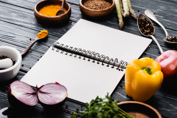 selective focus of fresh colorful vegetables and spices near blank notebook on wooden surface - Photo, Image