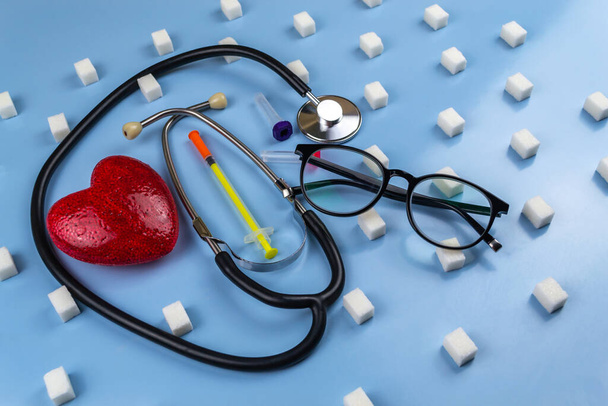 Стетоскоп, сердечный и инсулиновый шприц, окруженный кубиками сахара. Всемирный день борьбы с диабетом - Фото, изображение