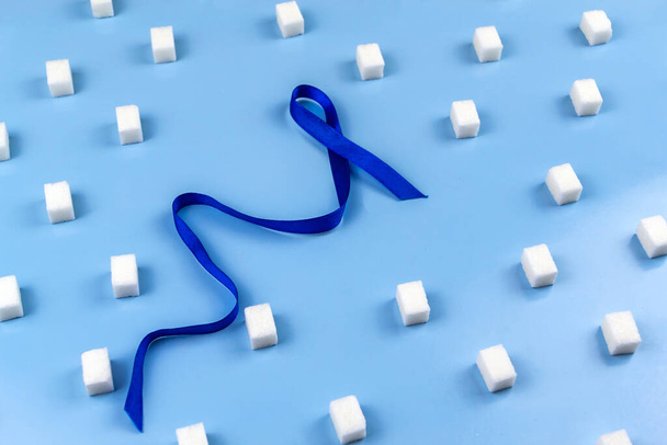Niebieska wstążka jest oznaką cukrzycy otoczonej kostkami cukru. Światowy Dzień Cukrzycy - Zdjęcie, obraz