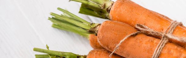 close up view of fresh carrots tied with rope on white wooden table, panoramic shot - Photo, Image