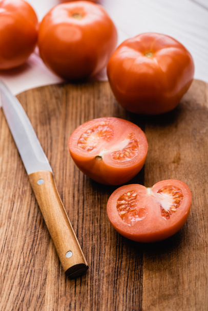 Tahta kesme tahtasının üzerinde bıçakla olgun domateslerin seçici odağı - Fotoğraf, Görsel