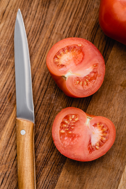 top view of ripe tomato halves on wooden chopping board with knife - Photo, Image