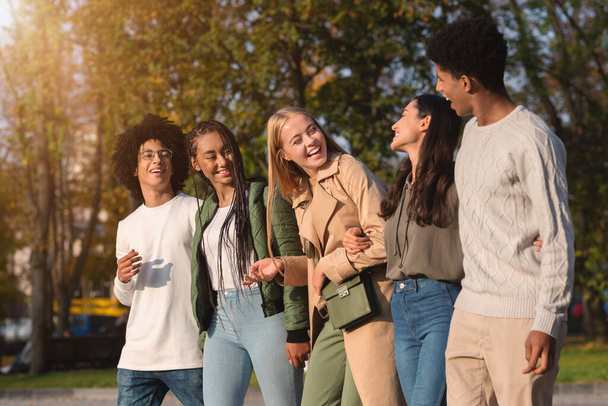 International group of teenagers laughing while walking by park - Photo, Image
