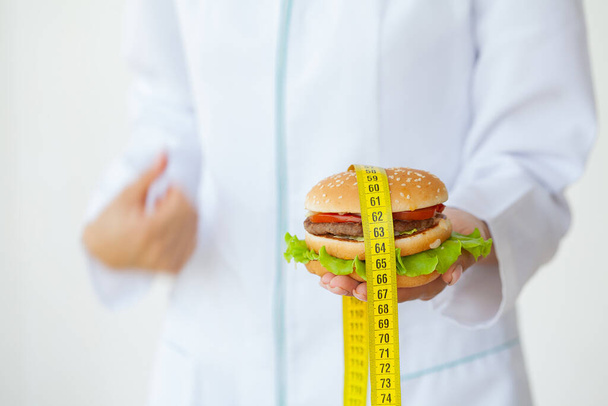 Diet concept, doctor holding harmful fat burger with yellow measuring tape - Fotoğraf, Görsel