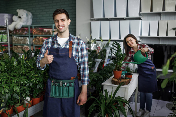 Gardeners happy boy and girl hold pots with plants in beautiful garden center, man showing okay sign. - Foto, Imagem