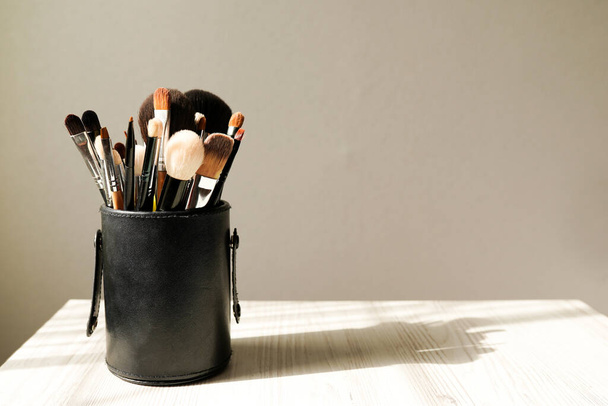 Make-up penselen in zwarte doos op lichte achtergrond met schaduw. Plaats voor tekst. - Foto, afbeelding