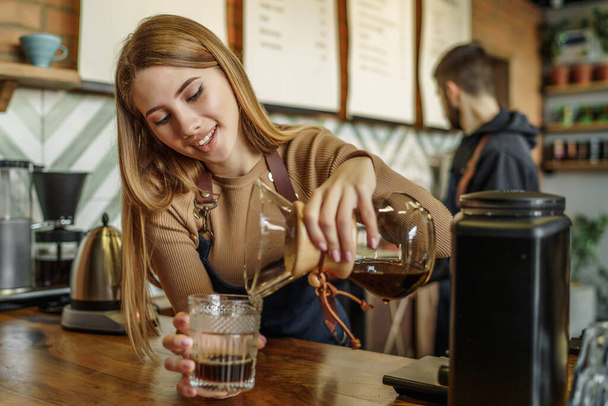 Cute women barista to make a drip brewing, filtered coffee, or pour over is a method which involves pouring water over roasted, ground coffee beans contained in a filter in a coffee shop. - Foto, Imagem